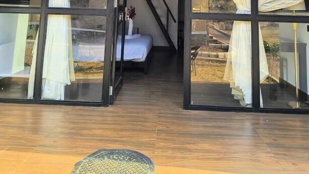 A modern, triangular-roofed structure with glass walls and white curtains, leading to a bed and a staircase.