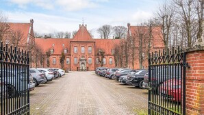 A paved driveway leading to a brick building with a red roof, surrounded by a metal fence and parked cars. - 4 Star Holiday Home in Skanderborg (Skanderborg)