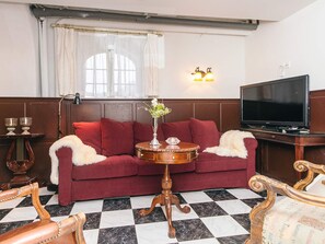 A room with a red sofa, a wooden side table with a vase, a black and white checkered floor, a television, and a wall-mounted light fixture. - 4 Star Holiday Home in Skanderborg (Skanderborg)