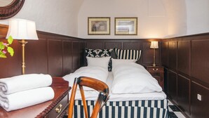 A neatly made bed with striped bedding, a wooden nightstand with a lamp, a chair, and a desk with a lamp and towels. - 4 Star Holiday Home in Skanderborg (Skanderborg)