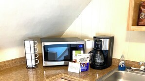 Ett kök med träskåp, en mikrovågsugn, en kaffebryggare och en flaska diskmedel från märket Dawn.