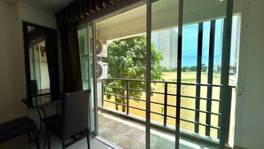 A room with a sliding glass door leading to a balcony with a view of a park and buildings. - Corner Studio With Balcony Near Jomtien Beach - Beach Mountain 6 (Pattaya)