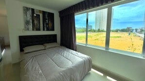 A bedroom with a large bed, a view of a beach, and a cityscape in the background. - Corner Studio With Balcony Near Jomtien Beach - Beach Mountain 6 (Pattaya)