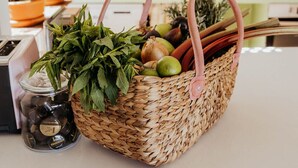 Ein Korbkörbchen mit Tragegriffen, gefüllt mit frischen Kräutern und Früchten, steht auf einer Küchenarbeitsplatte.