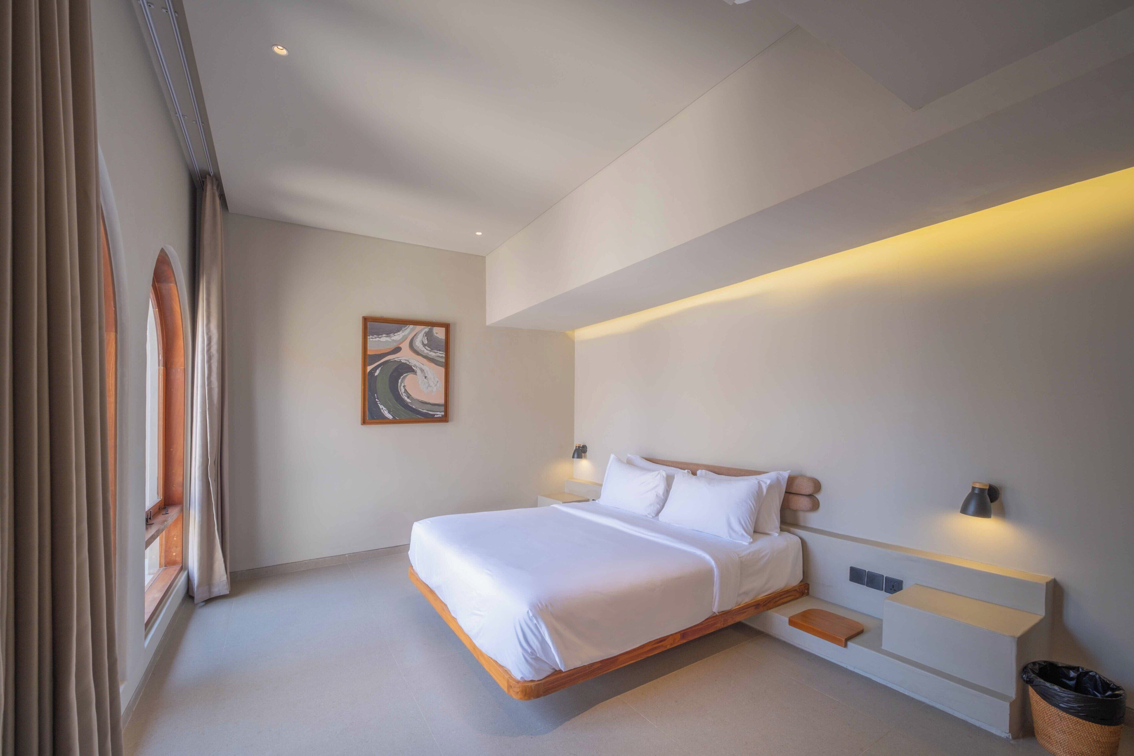 A modern bedroom with a large bed, bedside tables, a wall-mounted lamp, and a framed artwork.
