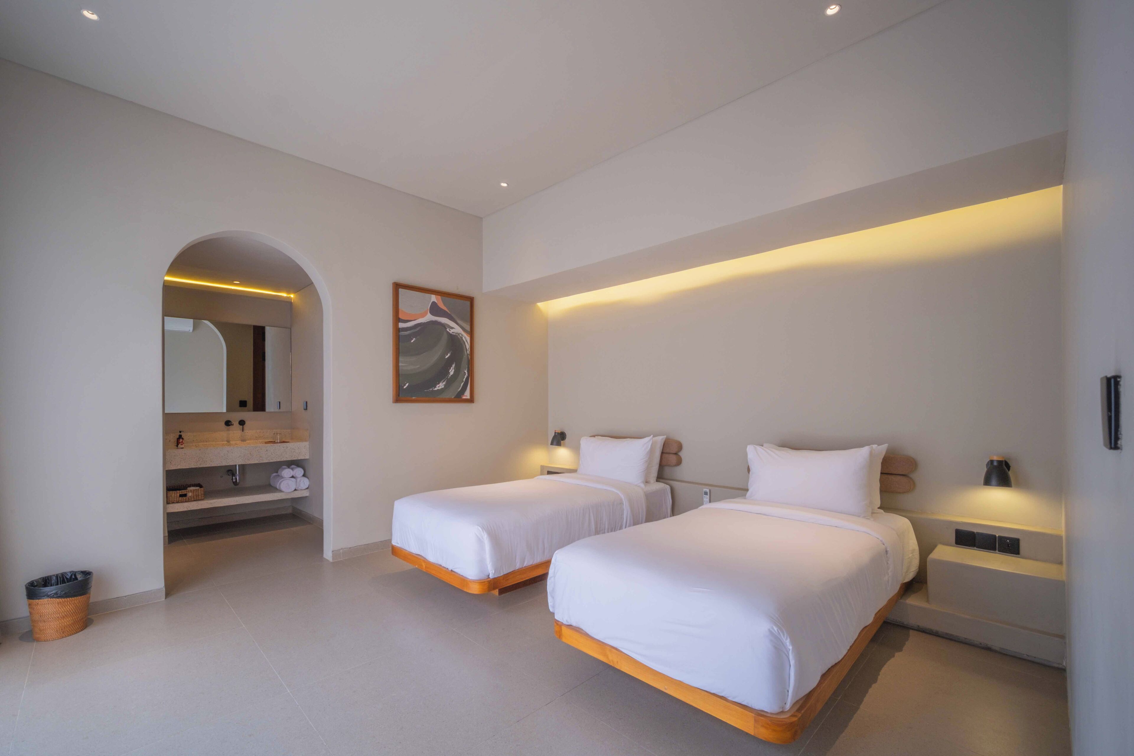 A modern hotel room with two single beds, a bathroom with a vanity, and a large mirror.