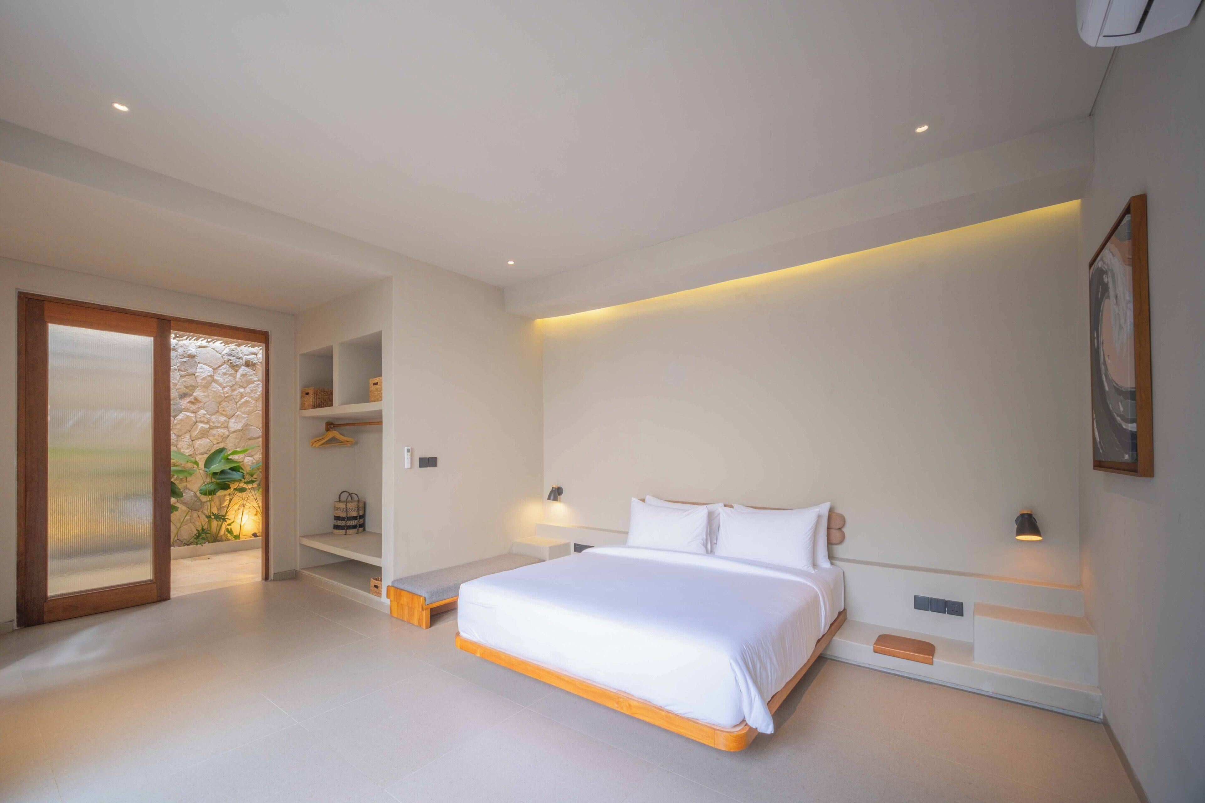 A modern bedroom with a large bed, built-in shelving, and a sliding glass door leading to a balcony.