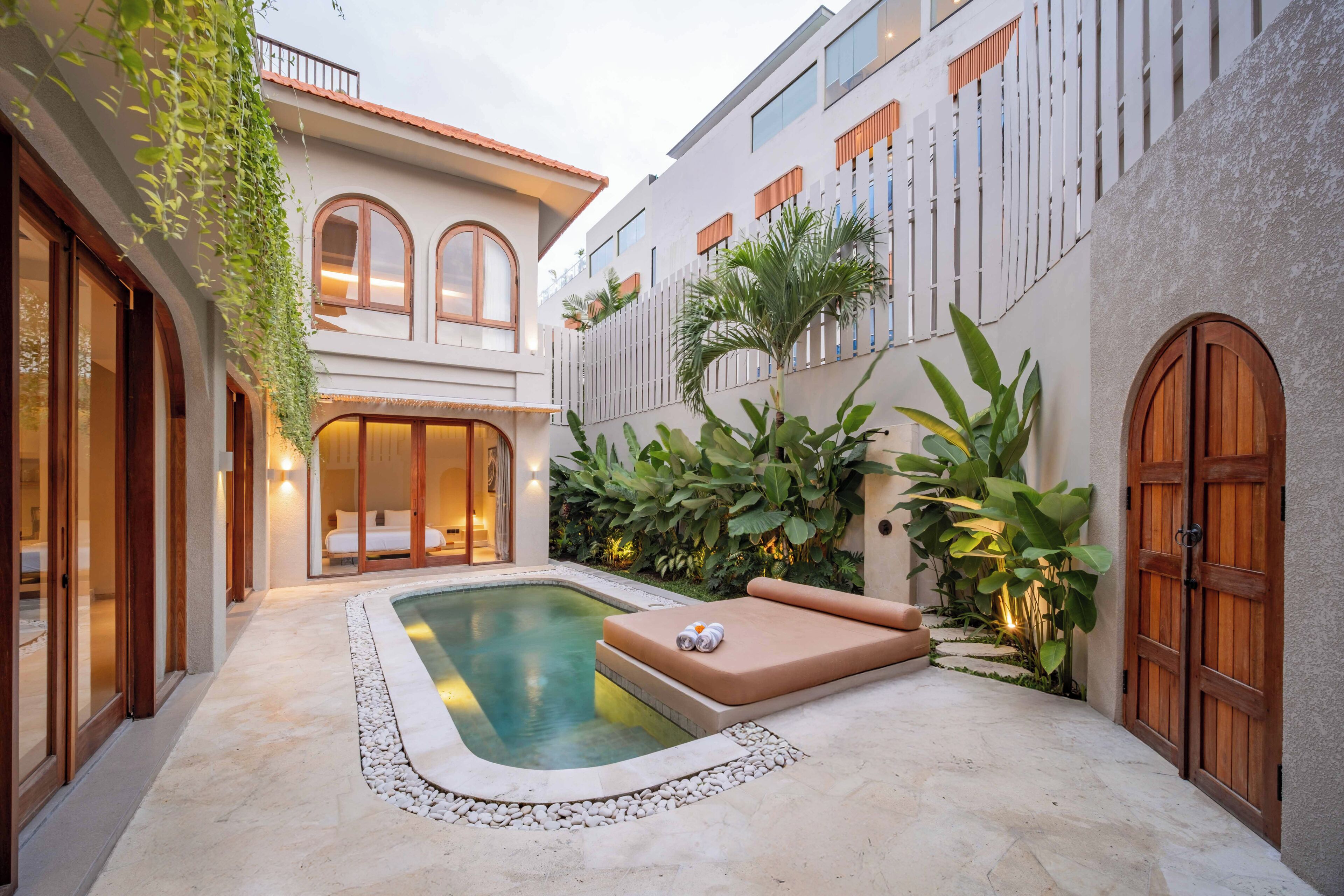 A courtyard with a swimming pool, a lounge area, and a building with large windows and a balcony.