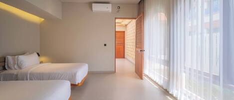 A hotel room with two beds, a large window with sheer curtains, and a wooden door leading to another room.