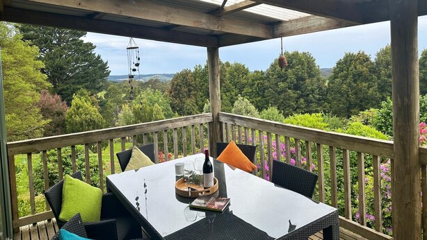 A covered outdoor seating area with a table set for two, surrounded by wooden railings and overlooking a lush landscape.