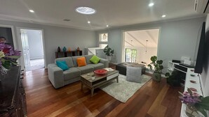 A spacious living room with a grey sofa, wooden coffee table, and a large window providing natural light.
