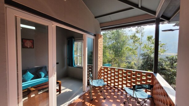 A balcony with a wooden floor, a cushioned seating area, and a view of trees and mountains.