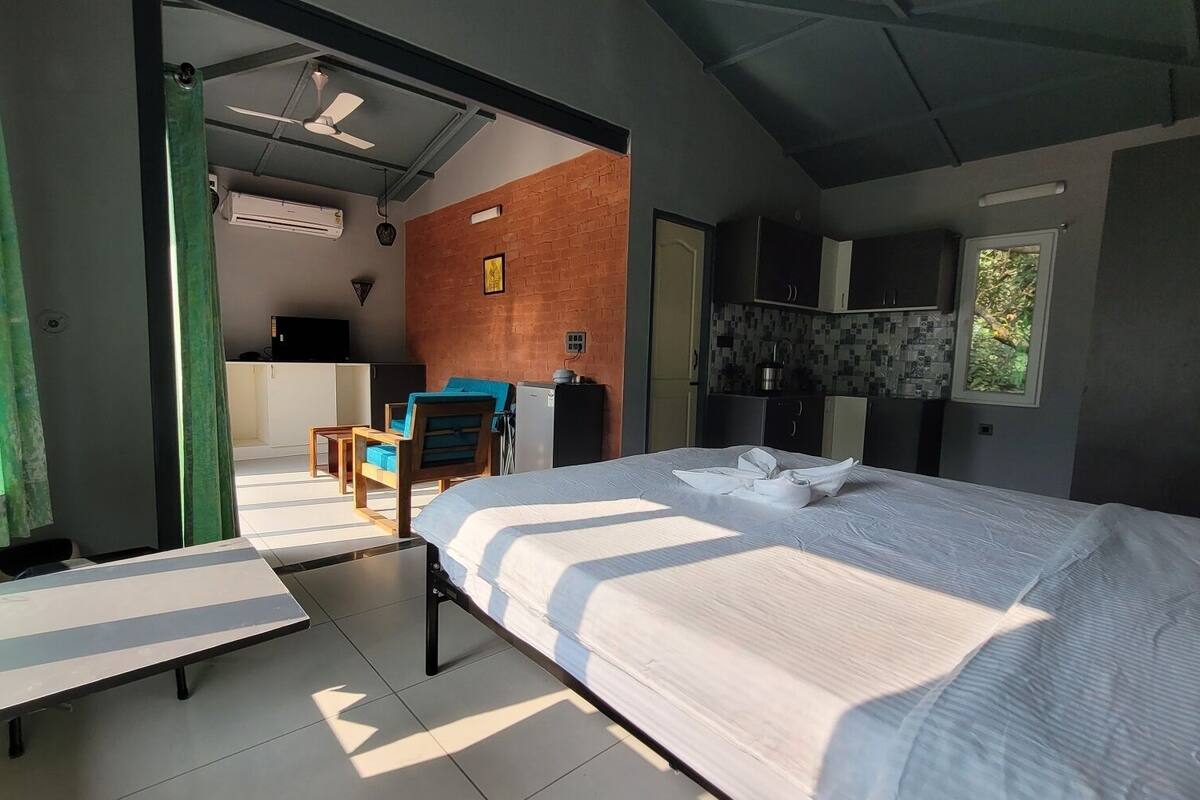 A modern hotel room with a large bed, a desk, and a kitchenette.