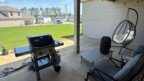 A covered patio with a grill, outdoor seating, and a hanging chair. - Modern 4-bedroom house for Masters Week (Grovetown)