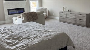 A bedroom with a bed, a TV mounted on the wall, a ceiling fan, a dresser, and a window. - Modern 4-bedroom house for Masters Week (Grovetown)