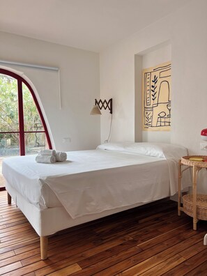Una camera da letto con un letto, una lampada a muro, un tavolino in vimini e un'ampia finestra.