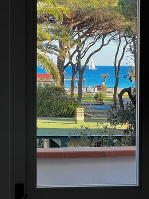 Vista di una spiaggia con palme, una barca a vela e un gazebo.