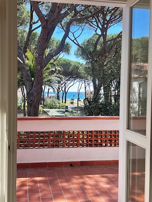 Un balcon doté d’un sol carrelé, d’une balustrade rouge et offrant une vue sur les arbres et la mer.
