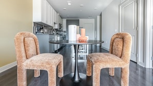 Een moderne keuken met roestvrijstalen apparatuur, een ronde eettafel met twee gestreepte stoelen en een witte deur op de achtergrond.