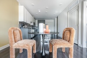 A modern kitchen with stainless steel appliances, a round dining table with two patterned chairs, and a white door in the background. - Blueground | Chevy Chase, rooftop, nr Glenview Park (Chevy Chase)