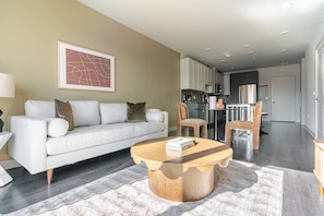 A modern living room with a sofa, coffee table, and chairs. There is a kitchen area in the background. - Blueground | Chevy Chase, rooftop, nr Glenview Park (Chevy Chase)