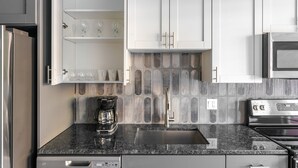 A modern kitchen with white cabinets, a granite countertop, a coffee maker, a stainless steel sink, and a microwave. - Blueground | Chevy Chase, rooftop, nr Rock Creek Park (Chevy Chase)