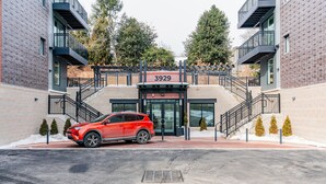 A modern building with a red SUV parked in front, featuring a prominent entrance and a staircase leading to the upper floors. - Blueground | Chevy Chase, rooftop, nr Rock Creek Park (Chevy Chase)