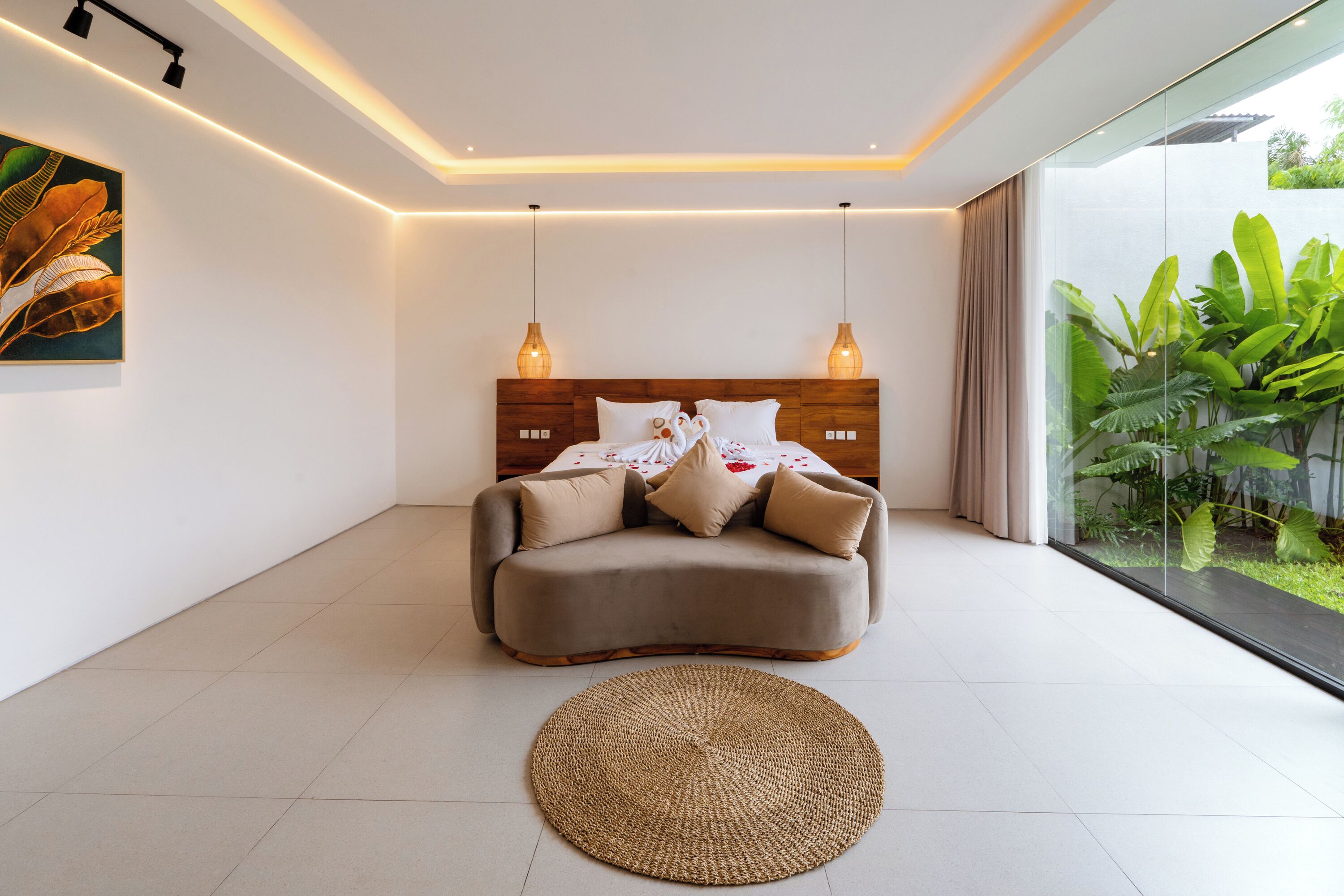 Une chambre moderne avec un canapé-lit aux lignes courbes, deux lampes suspendues, un tapis tissé et une grande fenêtre donnant sur un paysage verdoyant.
