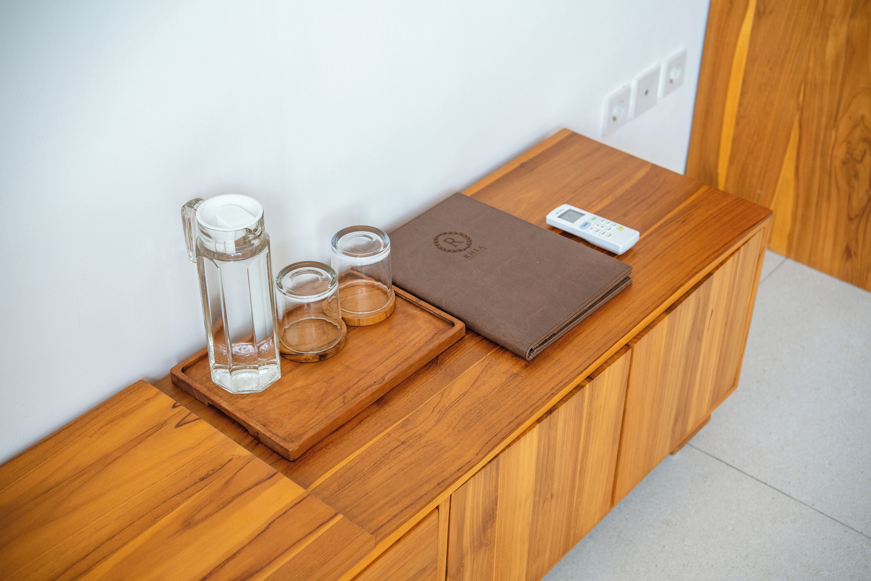 Una encimera de madera con una jarras de cristal, dos vasos y un libro encuadernado en cuero marrón.