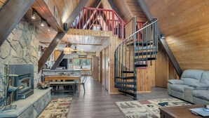A spacious loft with a high ceiling, a stone fireplace, a dining area, and a staircase leading to an upper level.