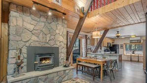 A cozy interior with a stone fireplace, wooden beams, a dining area, and a kitchen.
