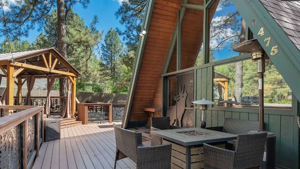 A wooden deck with wicker furniture, a covered seating area, and a view of the surrounding forest.
