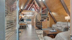 A spacious loft with a high ceiling, wooden beams, a staircase, a dining area, and a seating area with a sofa and a table.