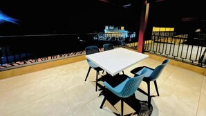 Un restaurante con una mesa blanca, sillas azules, suelo de baldosas y vistas de la ciudad de noche.