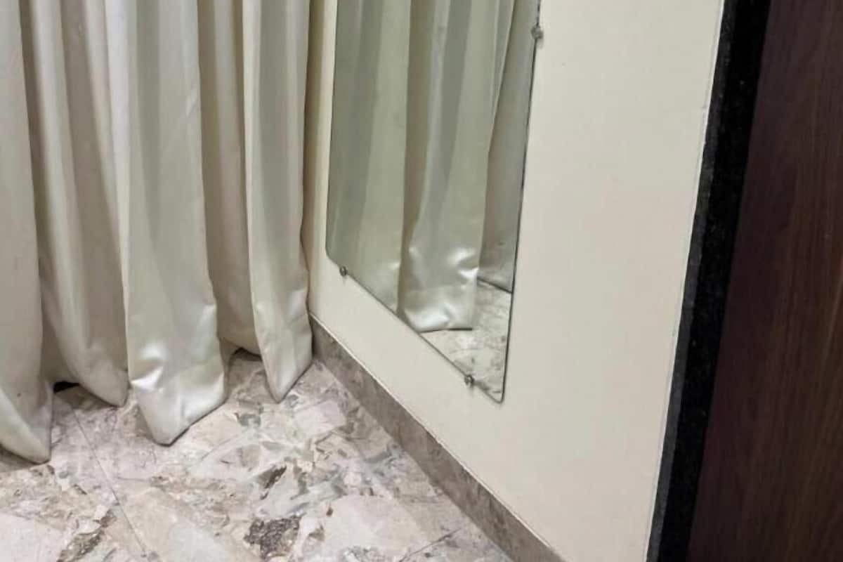 Une pièce avec un rideau, un miroir et un interrupteur sur le mur.