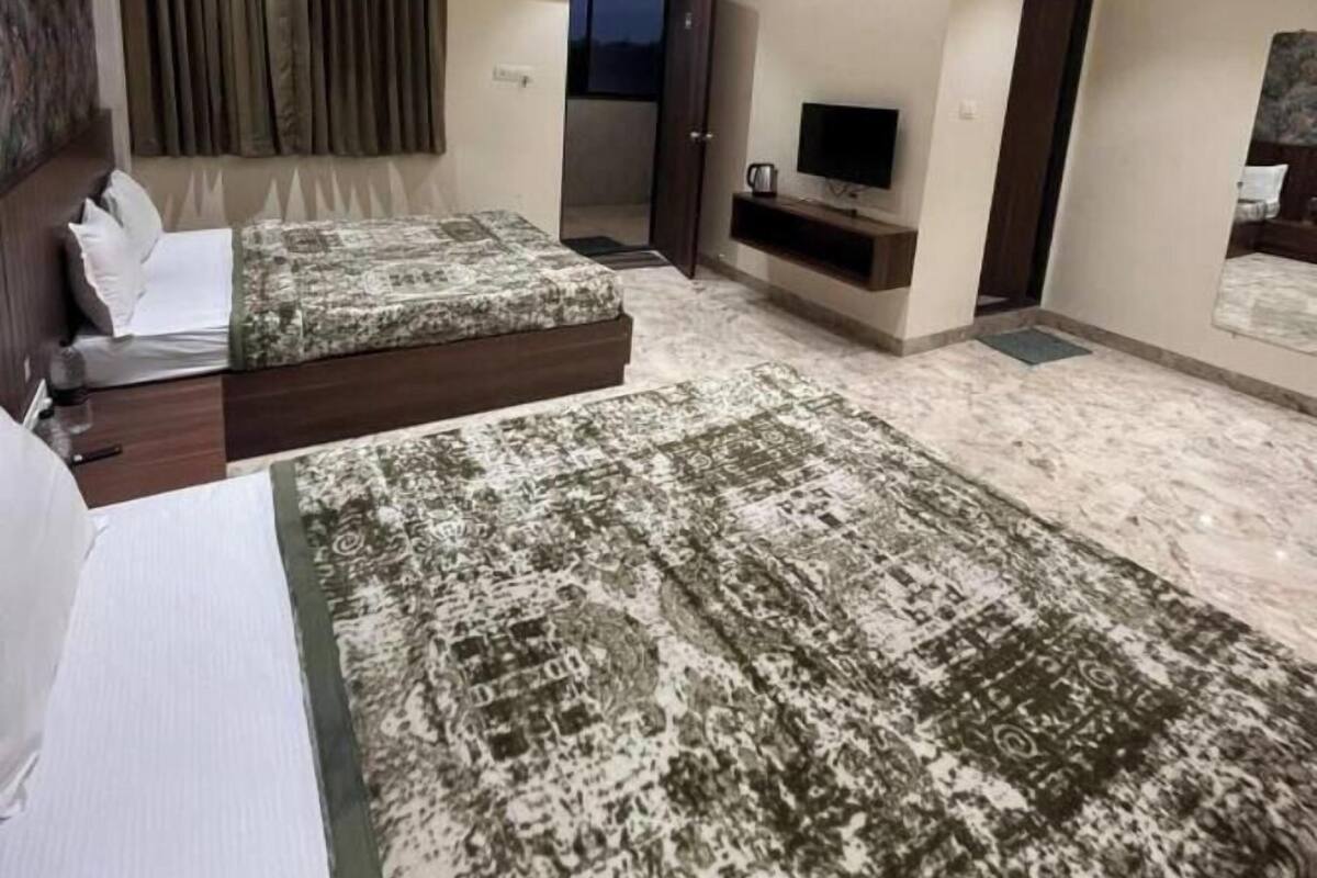 Une chambre d’hôtel moderne équipée de deux lits, d’un ventilateur de plafond, d’un éclairage encastré, d’un téléviseur à écran plat et d’une grande fenêtre avec des rideaux.