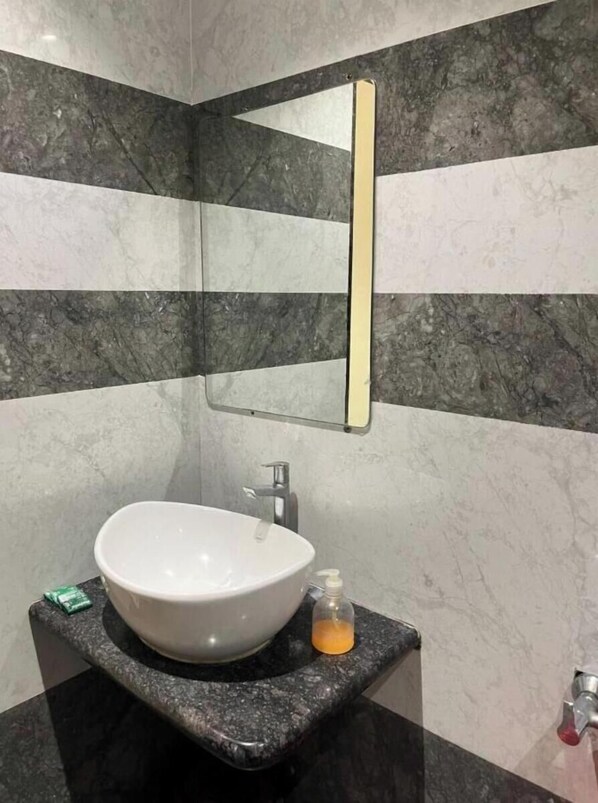 A bathroom with a white sink, a mirror, and a soap dispenser on a granite countertop. - Hotel Ashoka Resort (Khuldabad)