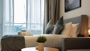Une chambre d’hôtel moderne avec un lit, un canapé, une table ronde en bois et une plante en pot.