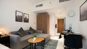 Un salon moderne avec un canapé gris, une petite table ronde en bois et un coin repas comprenant une chaise noire et une table dressée pour deux personnes.