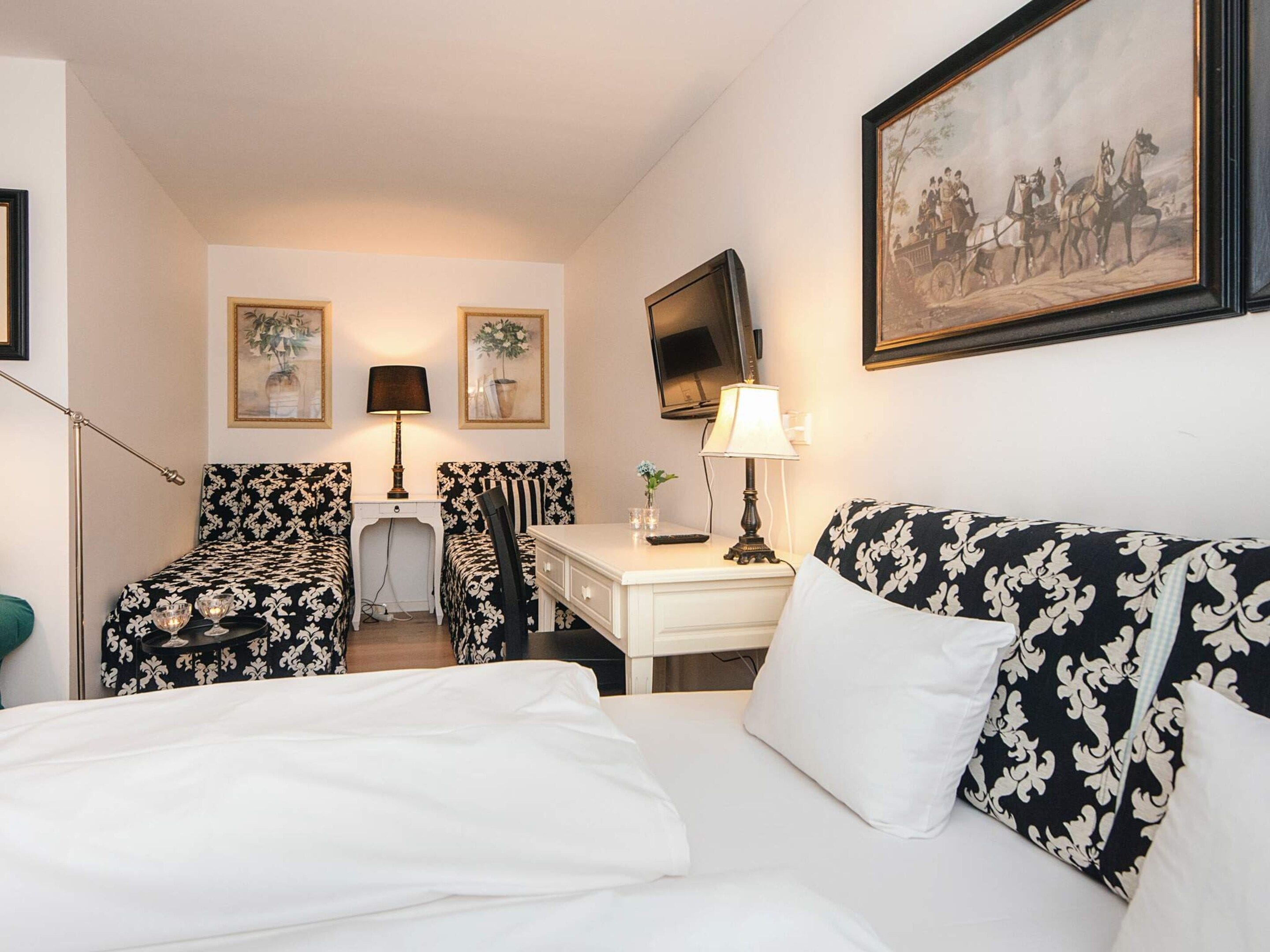 A hotel room with a bed, two armchairs, a desk, a television, and artwork on the walls.