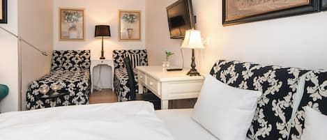 Ett hotellrum med en säng, två fåtöljer, ett skrivbord, en tv och konstverk på väggarna.