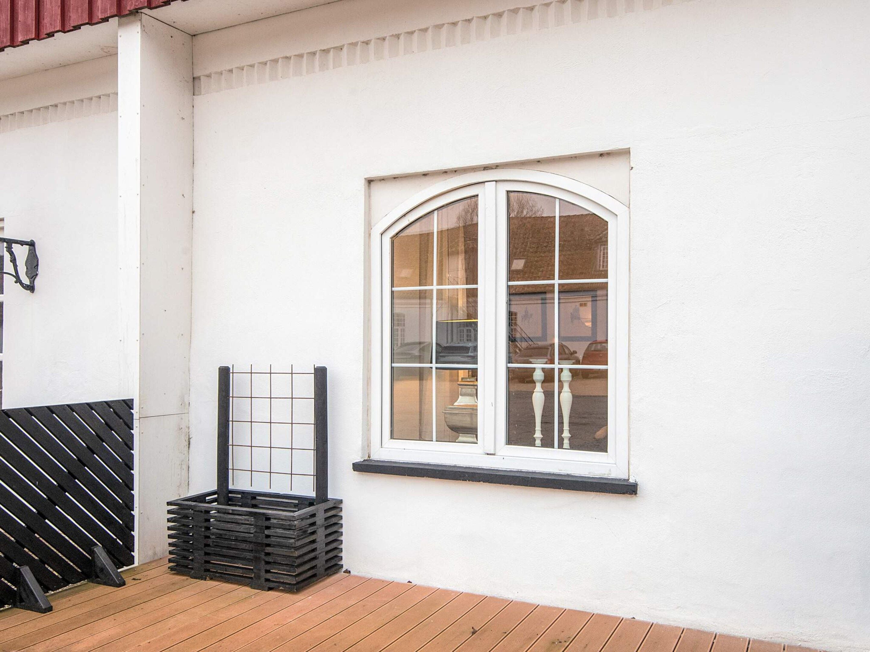 A white building with a single arched window, a black metal gate, and a stack of black crates.