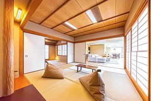 A traditional Japanese room with tatami flooring, a low wooden ceiling, and sliding doors leading to a living area with a sofa and a table. - Penthouse Ueno (Taito-ku)