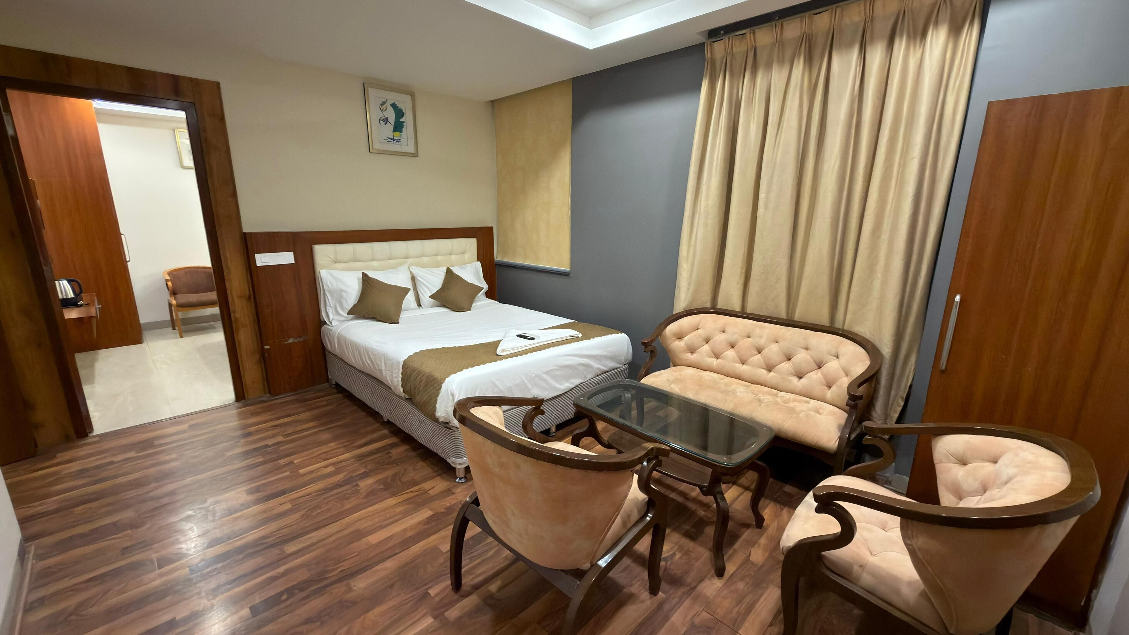 A hotel room with a bed, two armchairs, a glass coffee table, a wooden door, and a framed picture on the wall.