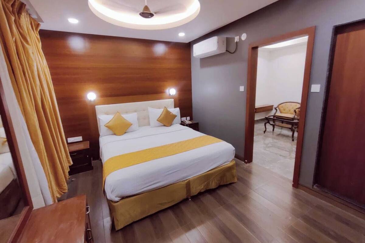 Een hotelkamer met een bed, houten lambrisering, een plafondlamp, een airconditioning en een stoel in de hoek.