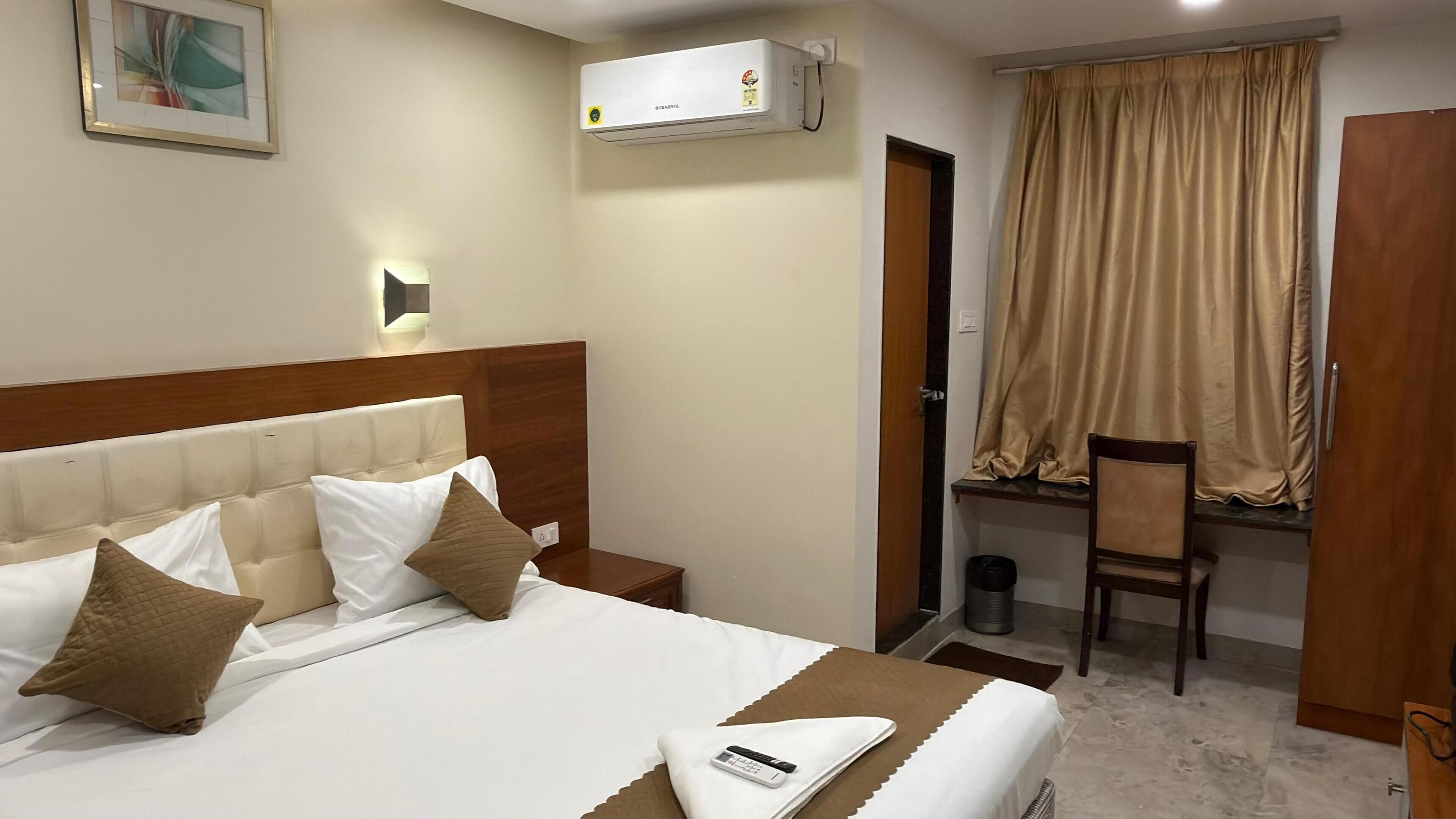 A hotel room with a bed, a desk, a chair, an air conditioner, and a curtain.