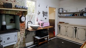 Una cocina con estufa antigua, un lavamanos, un microondas y una mesa de madera con un electrodoméstico rosa.