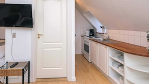 Een kleine keuken met witte kastjes, een houten aanrecht, een inbouwfornuis en een aan de muur bevestigde televisie.