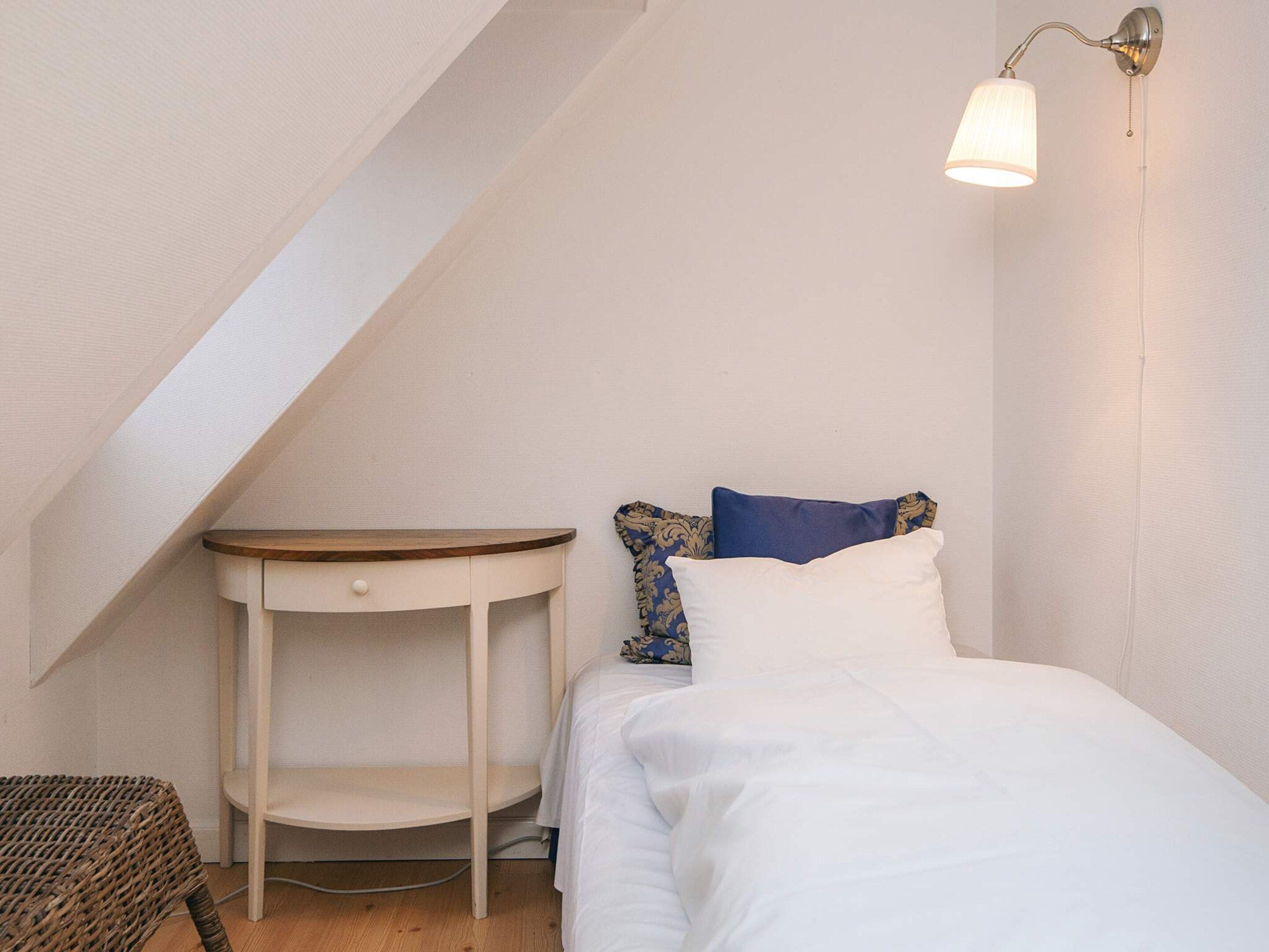 Une petite chambre à coucher accueillante, avec un lit simple, une table de chevet, une lampe et une chaise.