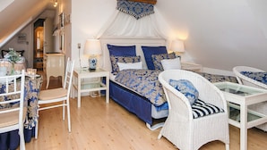 Een slaapkamer met een bed, twee witte rieten stoelen, een klein tafeltje en een nachtkastje met lampen.